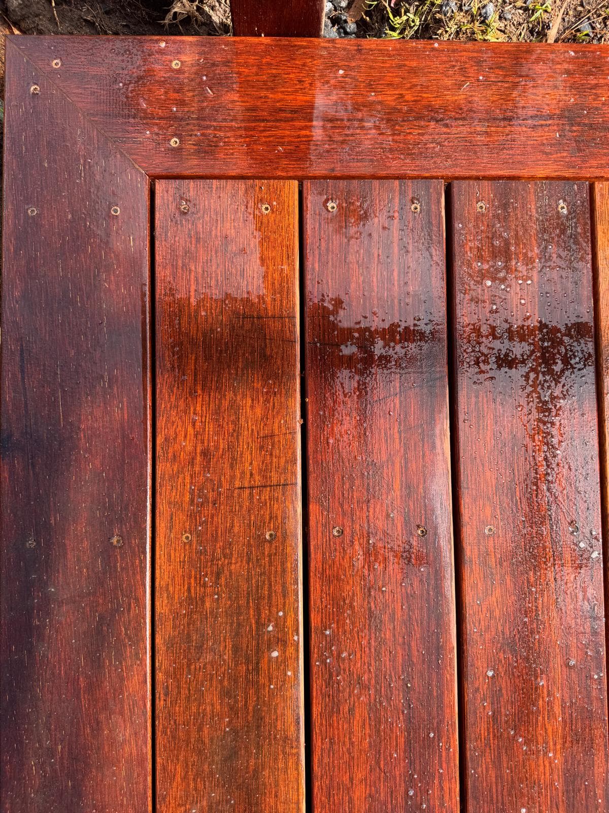 Wet, dark reddish-brown wooden deck planks with visible water droplets and a mitered corner.