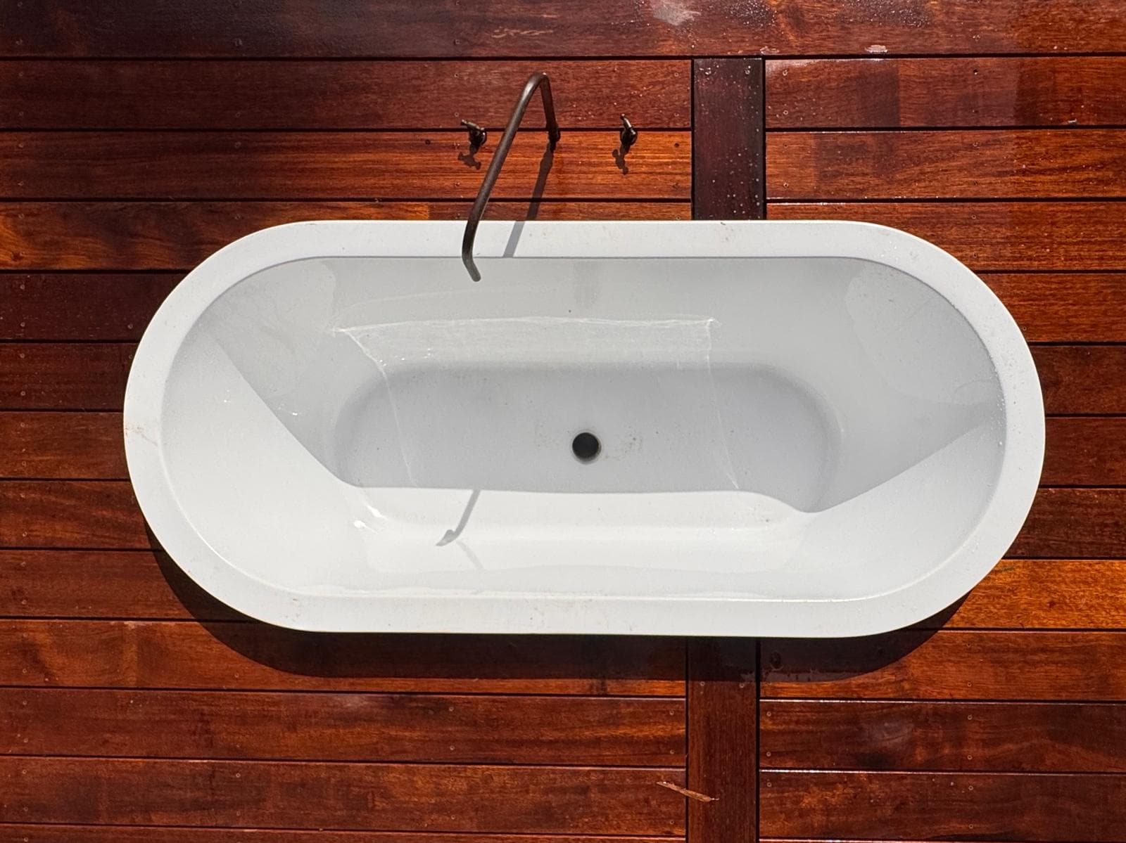 White oval bathtub on a dark wood deck, viewed from above with a minimalist faucet.