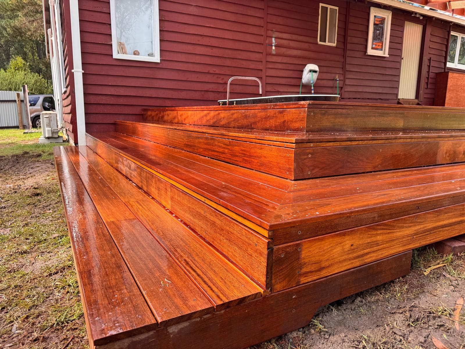 Glossy reddish-brown wooden steps wrap around the corner of a red-sided house.