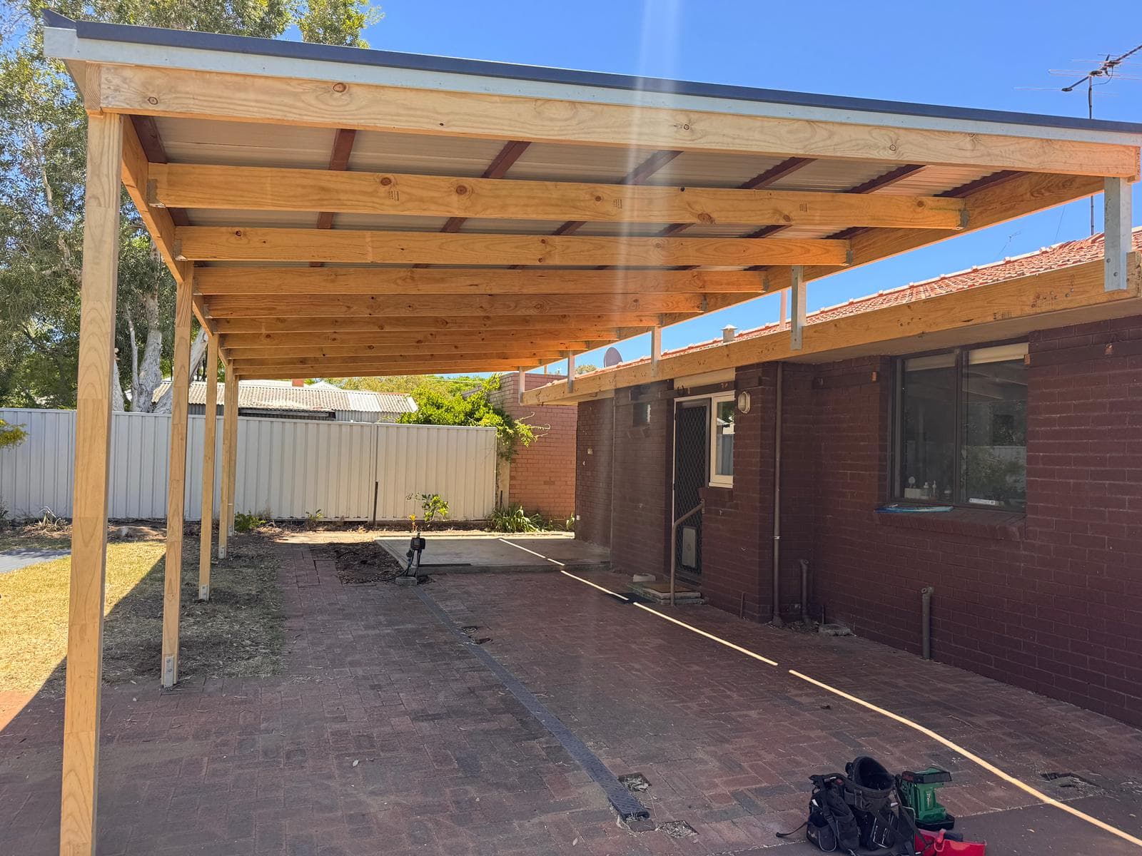 Sturdy wooden patio structure with metal roofing attached to a brick house over paved ground.