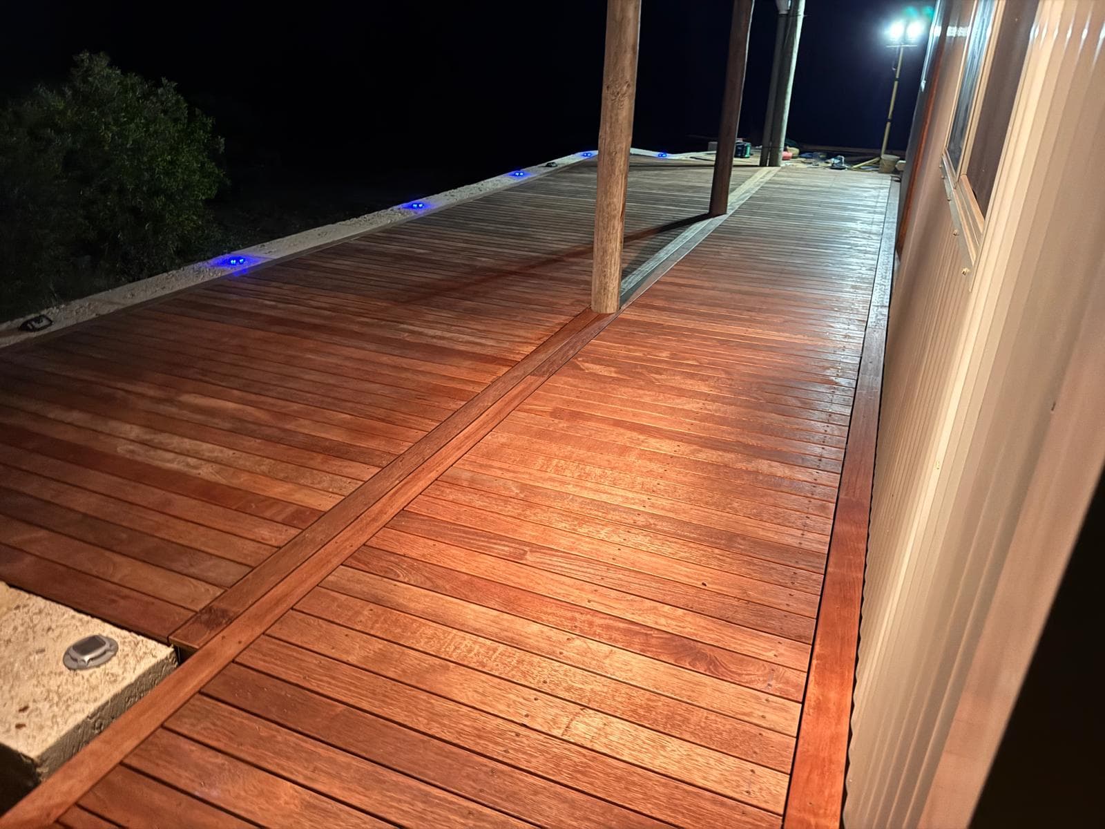 Reddish wooden deck at night with blue LED lights along the edge and support beams.