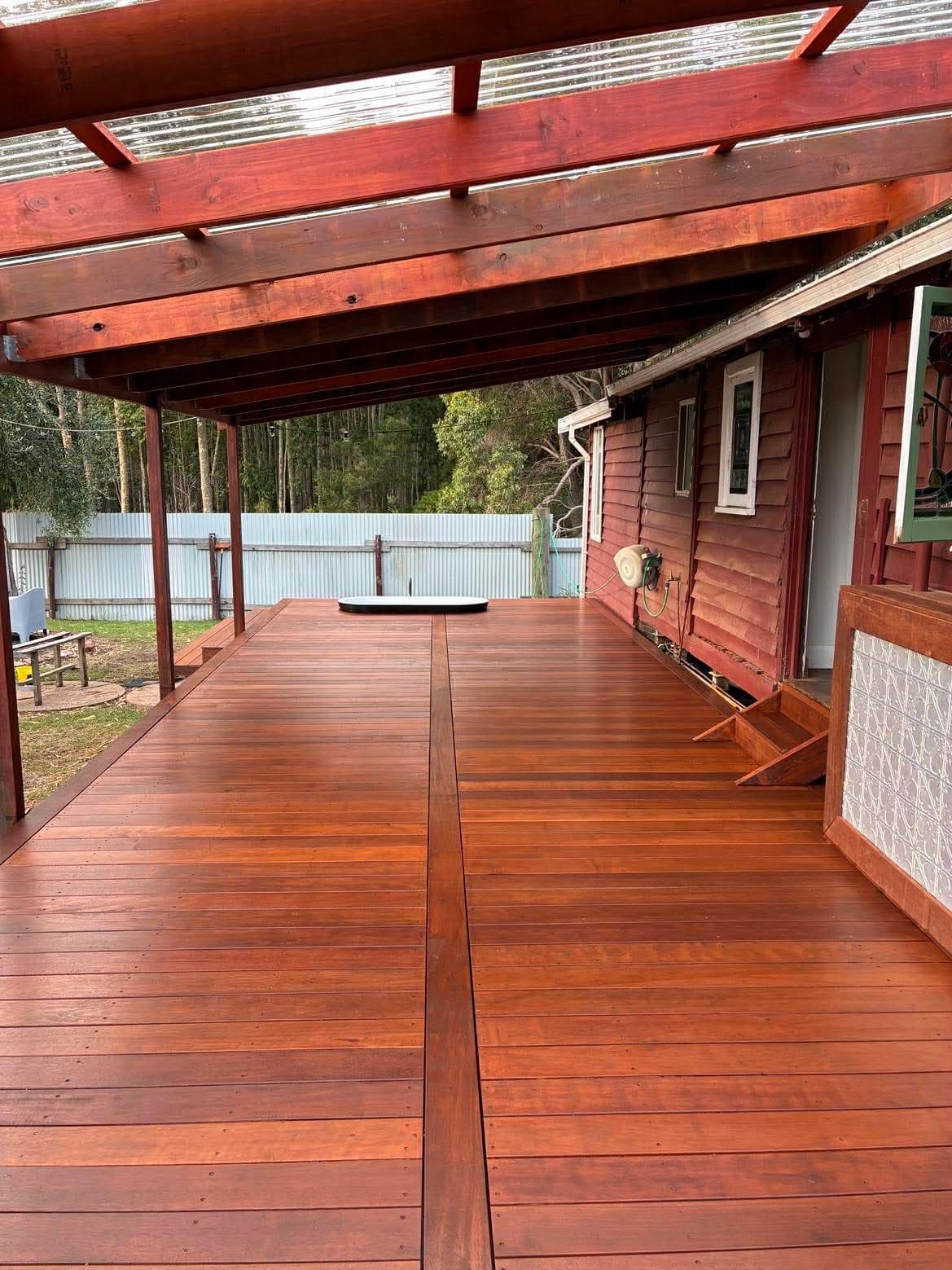 A polished reddish-brown wooden deck under a translucent roof attached to a red house.