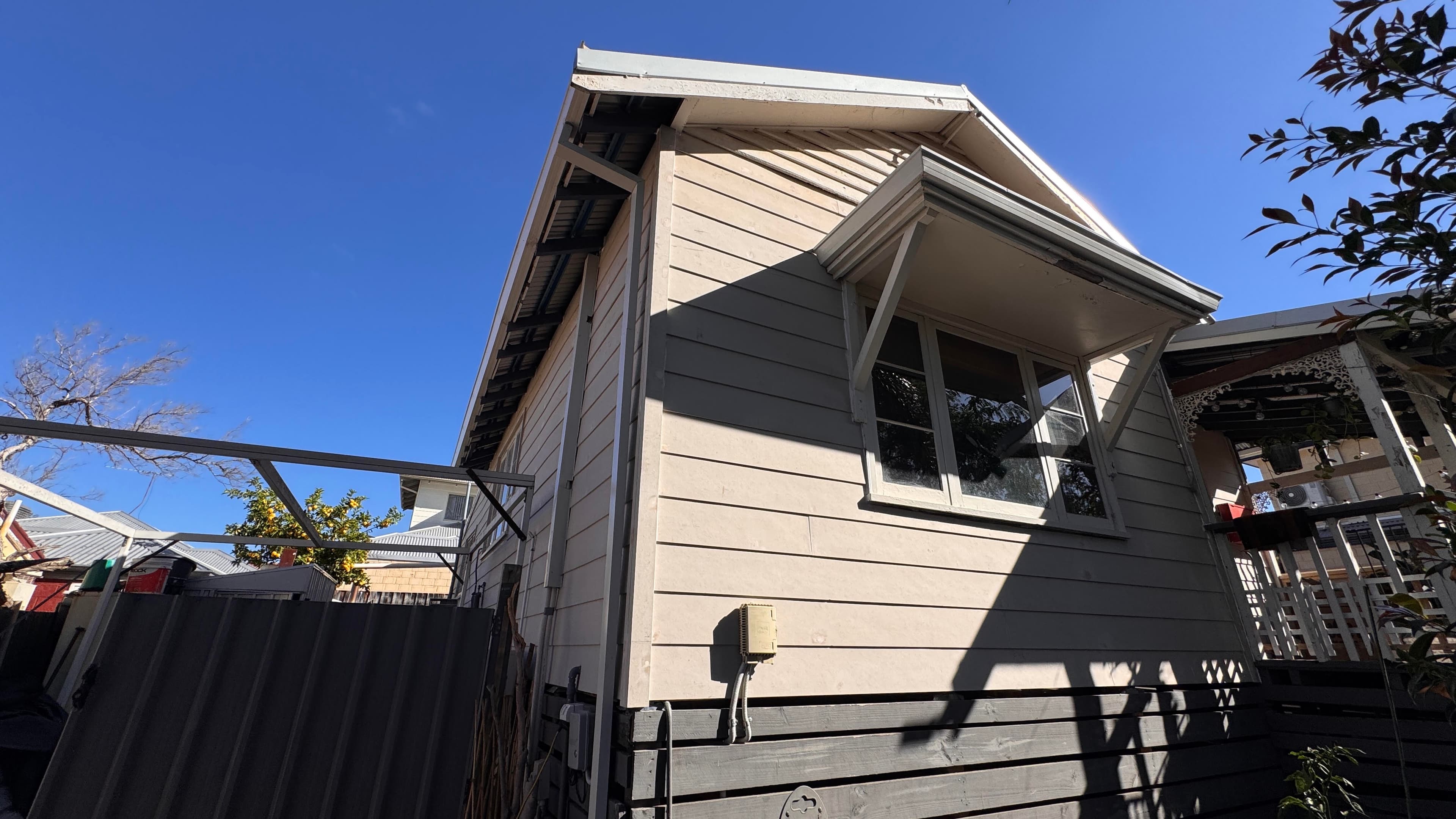 Beige weatherboard house featuring a window awning and dark baseboards against a clear blue sky.